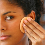 Woman with dark skin applying foundation makeup