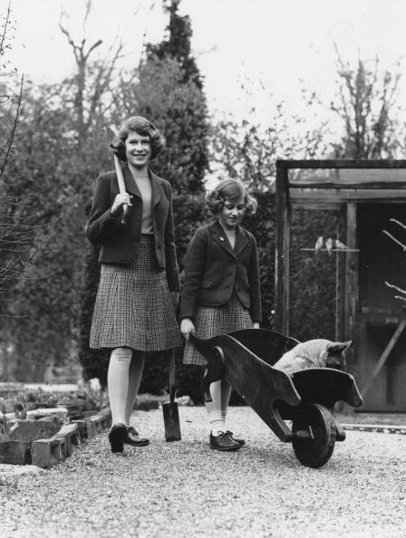 Princess Elizabeth (now Queen Elizabeth II, left) and her younger sister Princess Margaret Rose (1930-2002) in their garden at the Royal Lodge in Windsor Great Park, April 1940. The passenger in the wheelbarrow is a corgi named Carol