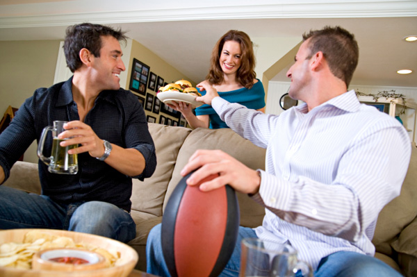 Woman serving hamburgers to husband and friend watching football