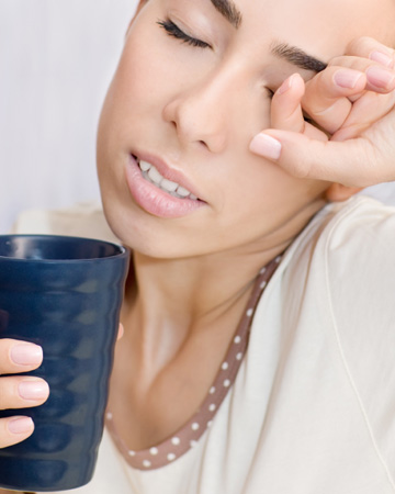 Woman drinking coffee and rubbing eyes