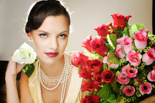 Woman with a pearl necklace holding a rose.