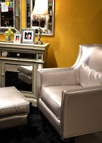 The mirrored table, yellow wall, and fringed lampshades combined with the nailhead trimmed chair gives this vignette a modern Hollywood Regency feel.