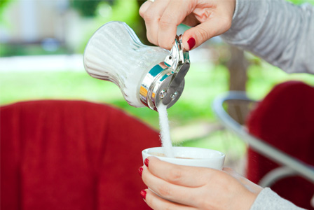 Woman pouring sugar into coffee