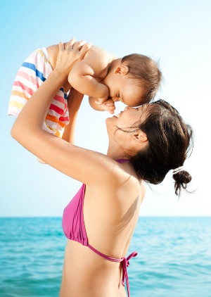 mother holding baby up at beach