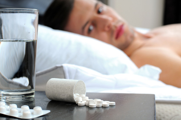 Man in bed looking at pills