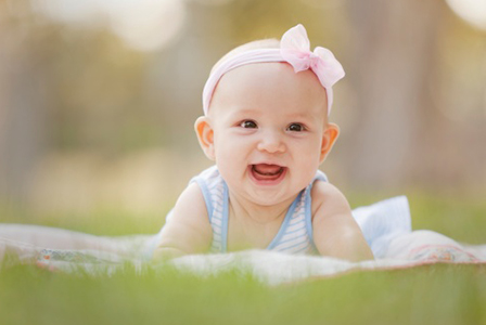 Smiling baby girl laying in grass | Sheknows.com