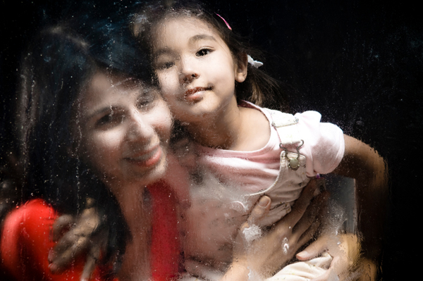 Woman and daughter looking through rainy window