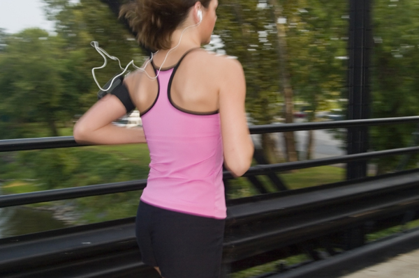 Woman with earbuds running over bridge